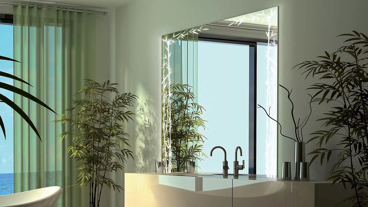 Snippet of a lighted mirror that is set above a basin with a dwarf bamboo tree on the side.