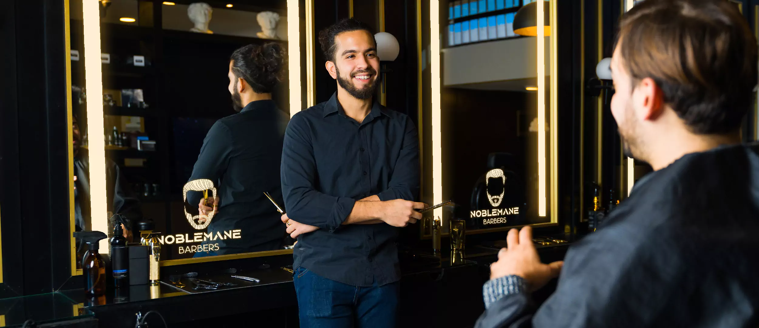 Two men having conversation in a barber shop, and a mirror with a LED light logo shown in Brisbane.