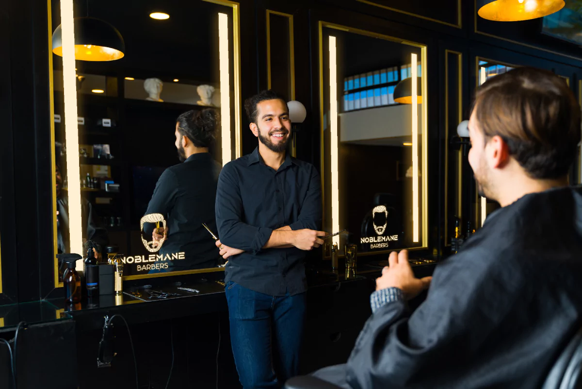 Two men having a talk in a barber shop reflected in a mirror with a lighted logo in Victoria.