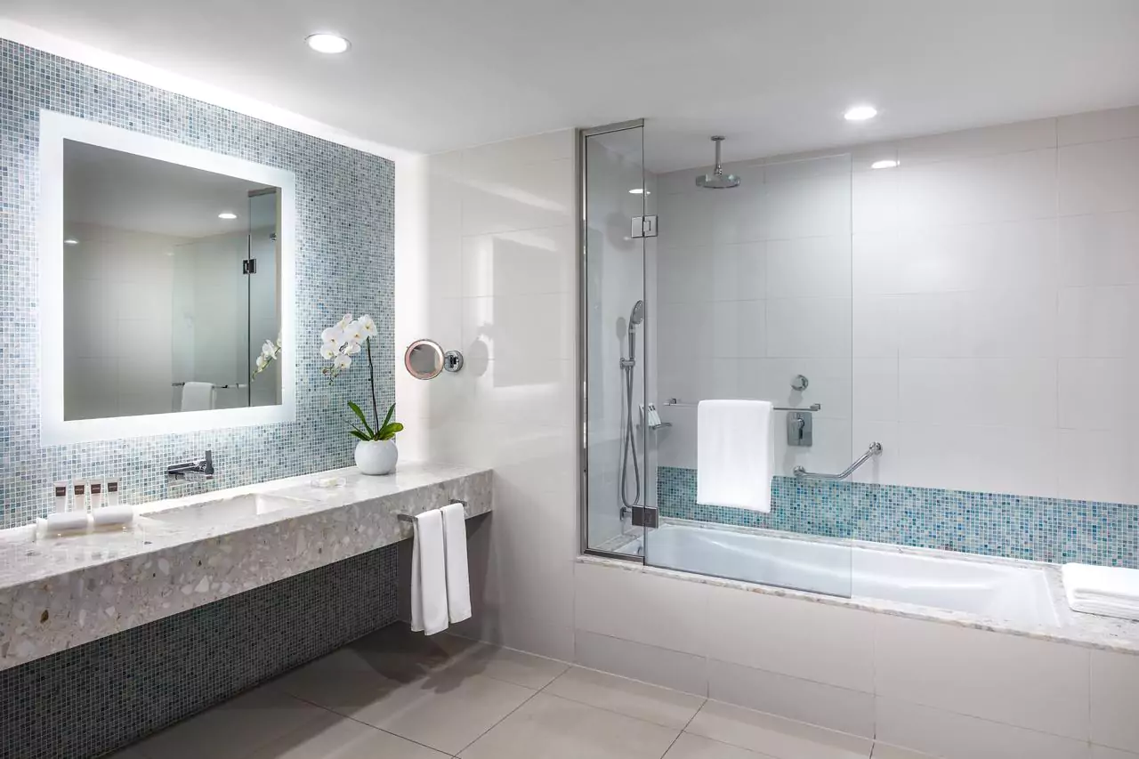 Tiled bathroom with bathtub, sink, and illuminated frosted mirror in Victoria.