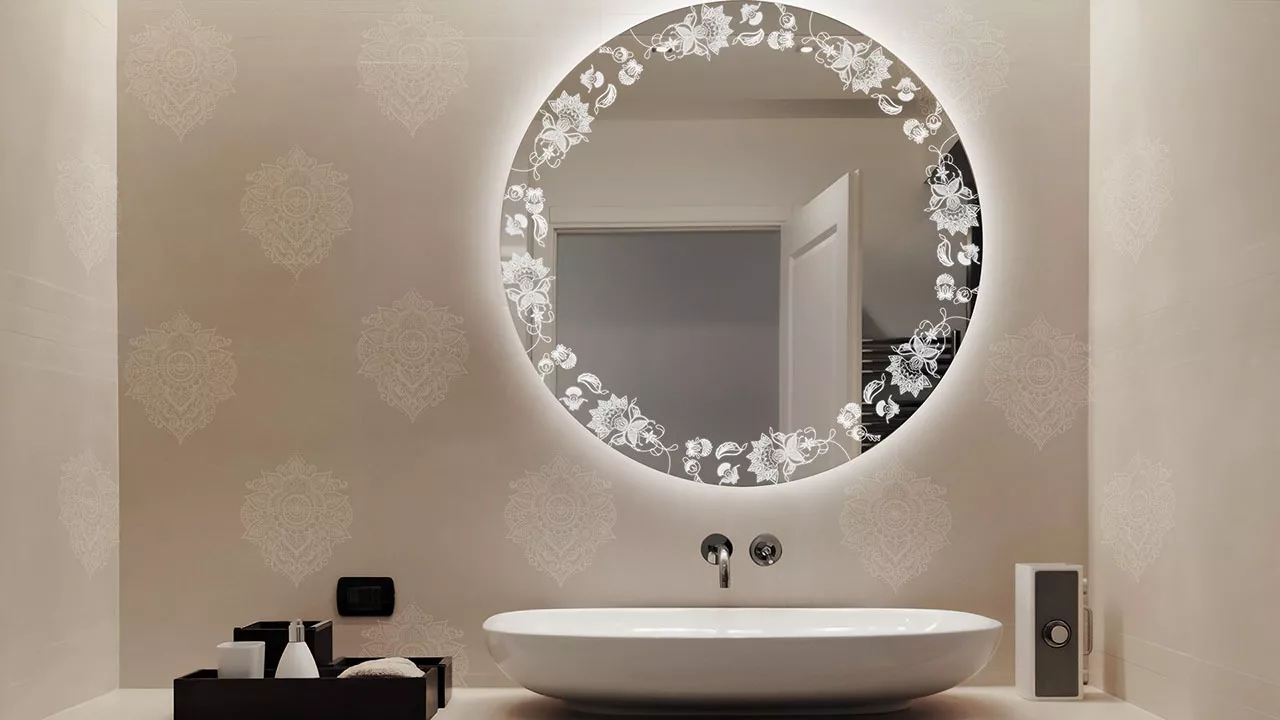 A snippet of a round-shaped backlit mirror above a single white washbowl and sink.