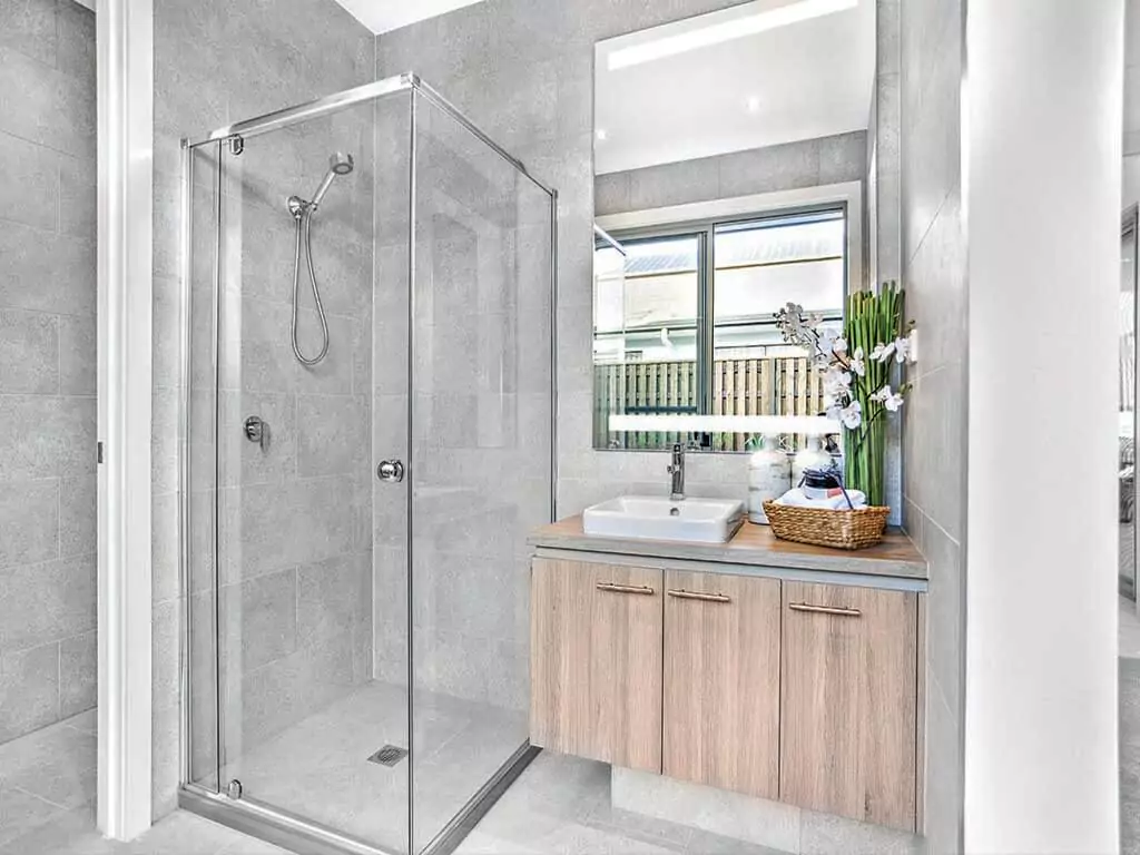 A modern bathroom featuring a glass shower room, and a sink with a lighted mirror in Canberra.