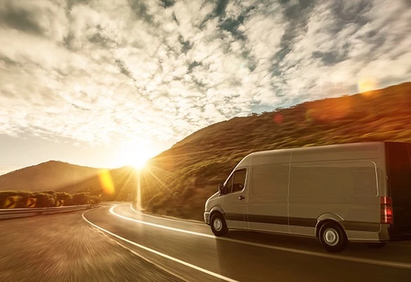 Van in Newcastle drives on a road at sunset, with the colorful sky as its backdrop.