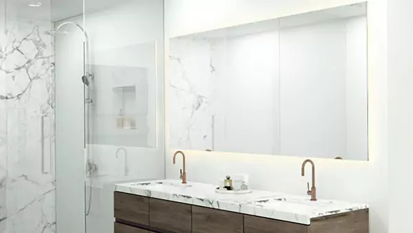  A modern bathroom with marble walls and a wide backlit mirror in Sydney.