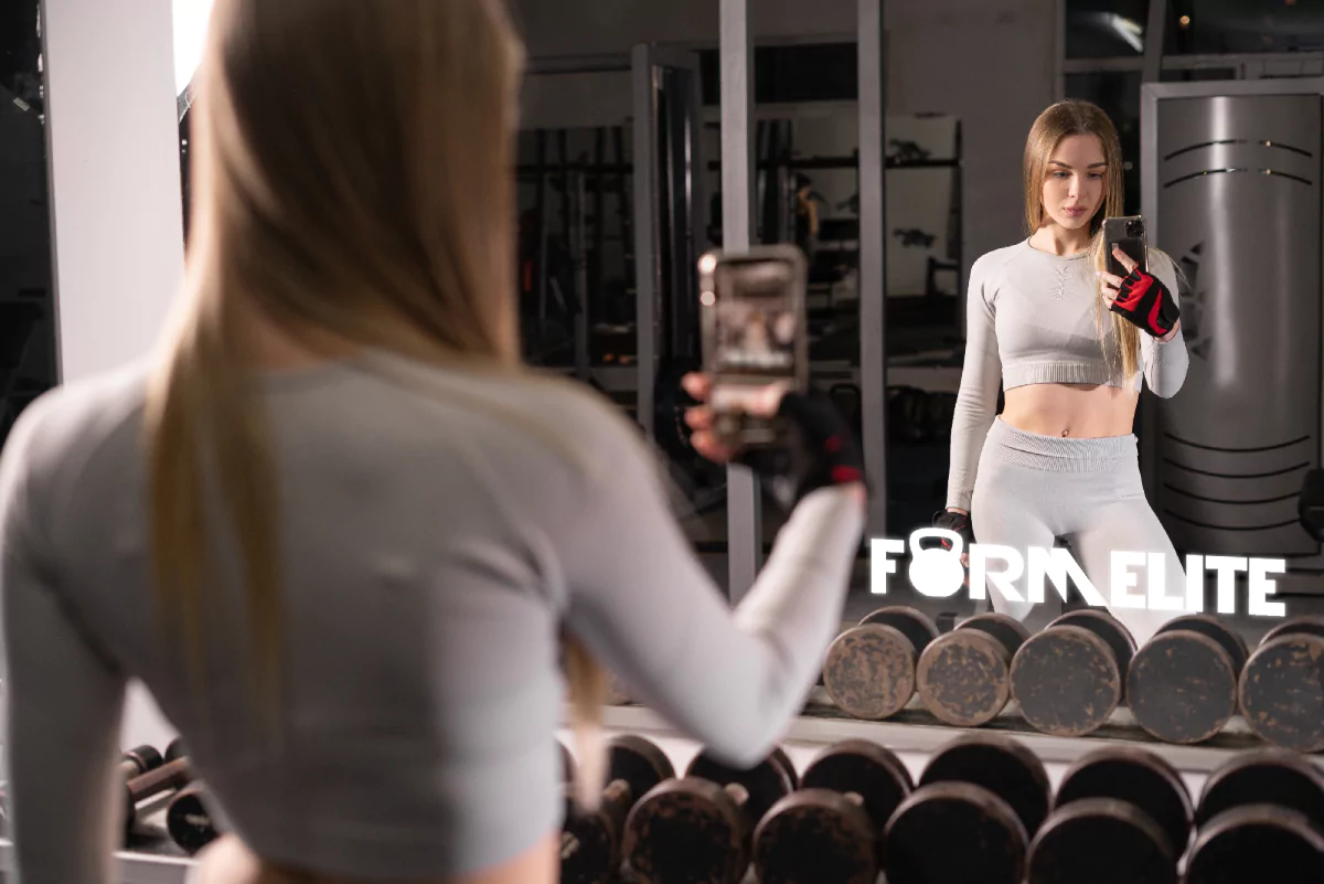 A woman in a gym, capturing a selfie in front of a mirror with a lighted logo in Melbourne.