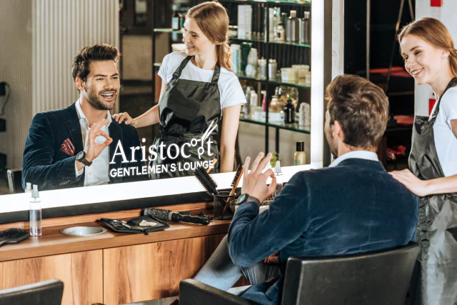 An icon of a woman admiring a man's hair reflecting in a mirror with a lighted logo in Brisbane.