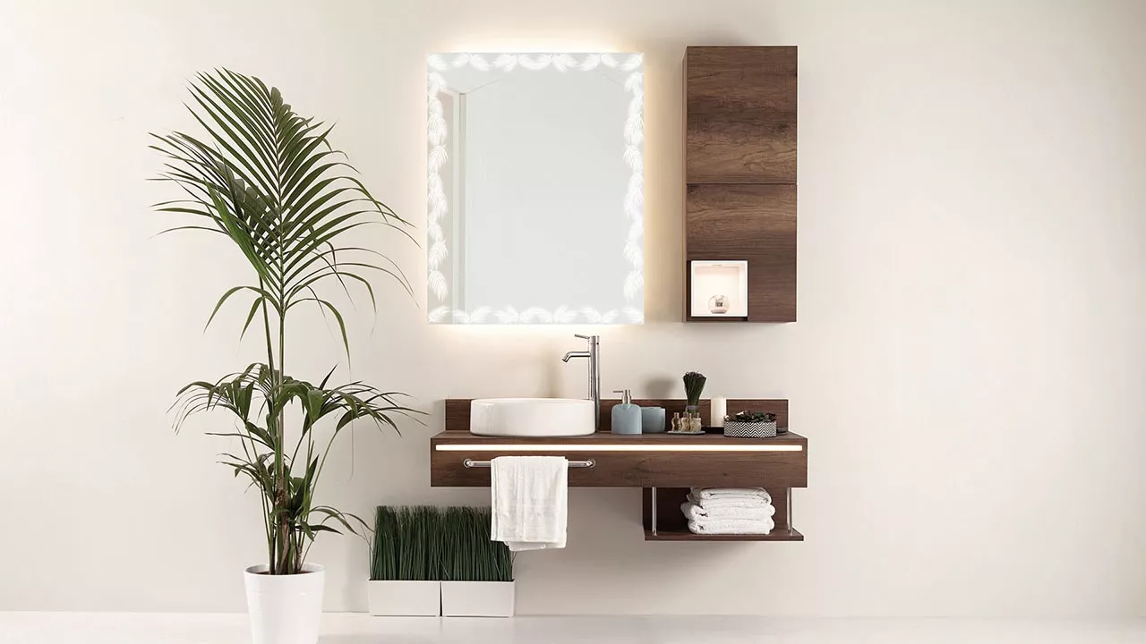 Thumb of a lit wall-mounted mirror featuring a tropical leaf design with palm tree in a washroom.