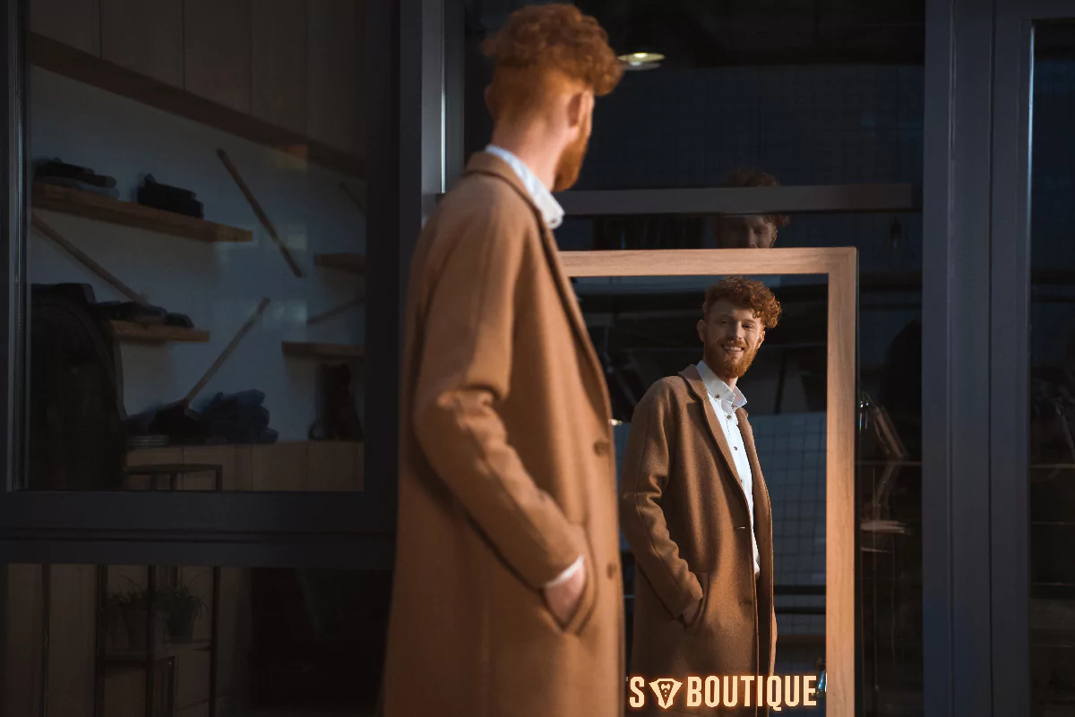 Man in coat gazing at his reflection in a mirror featuring a custom illuminated logo in Adelaide.