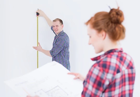 A man in Melbourne measuring the wall while looking at the woman holding a sketch plan.