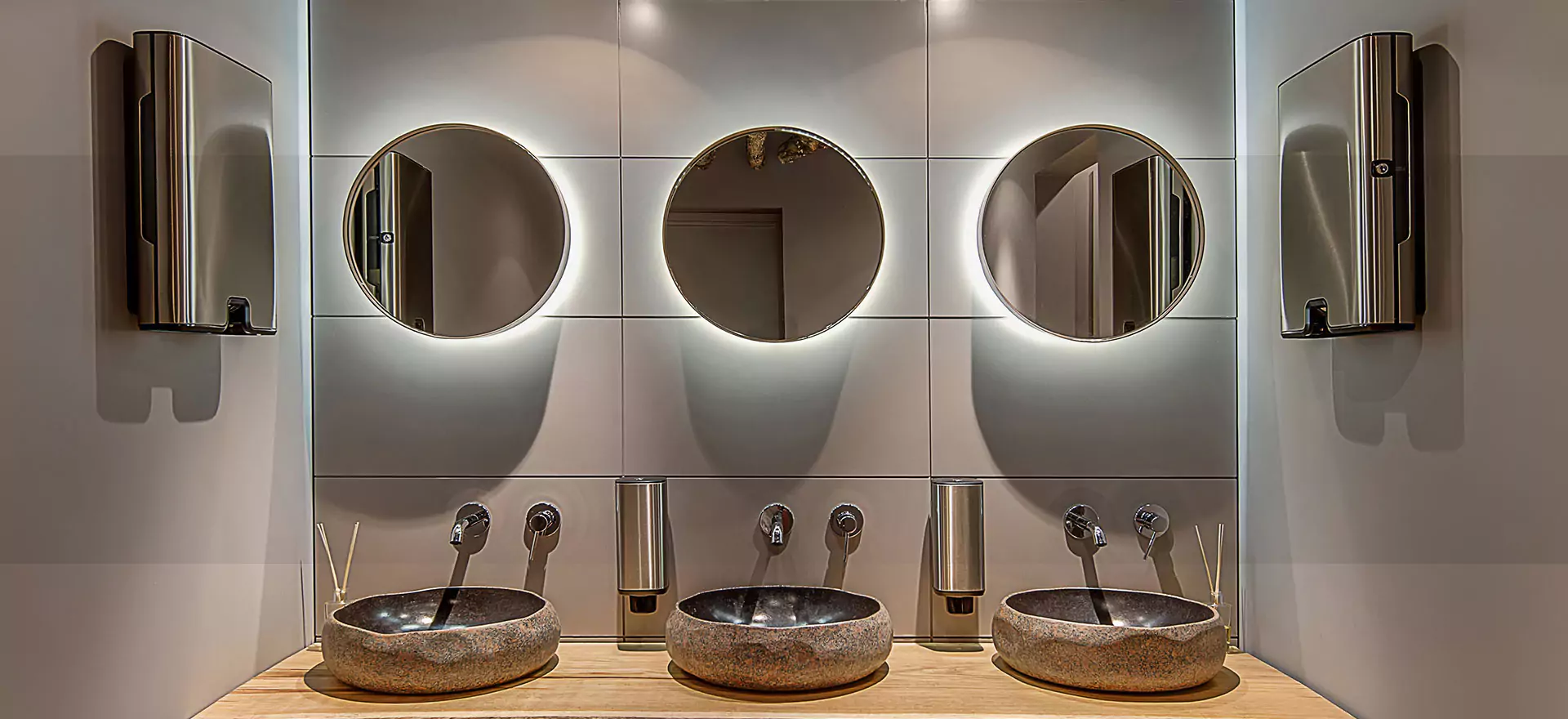 Three sinks and lighted mirrors in a spacious bathroom, ideal for a busy morning routine in Canberra.