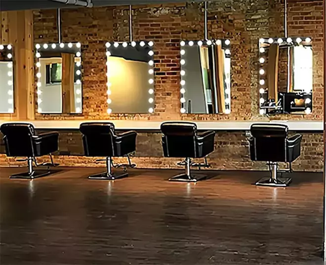 Salon with sleek chairs and wall-mounted lighted mirrors arranged on brown brick walls.