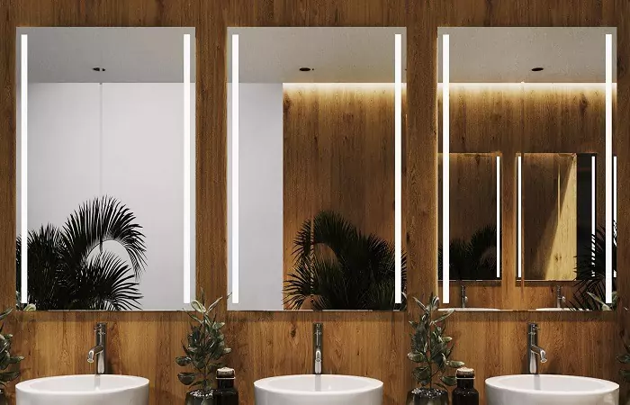 Lighted mirrors above three sinks installed against wooden walled bathroom in Victoria.